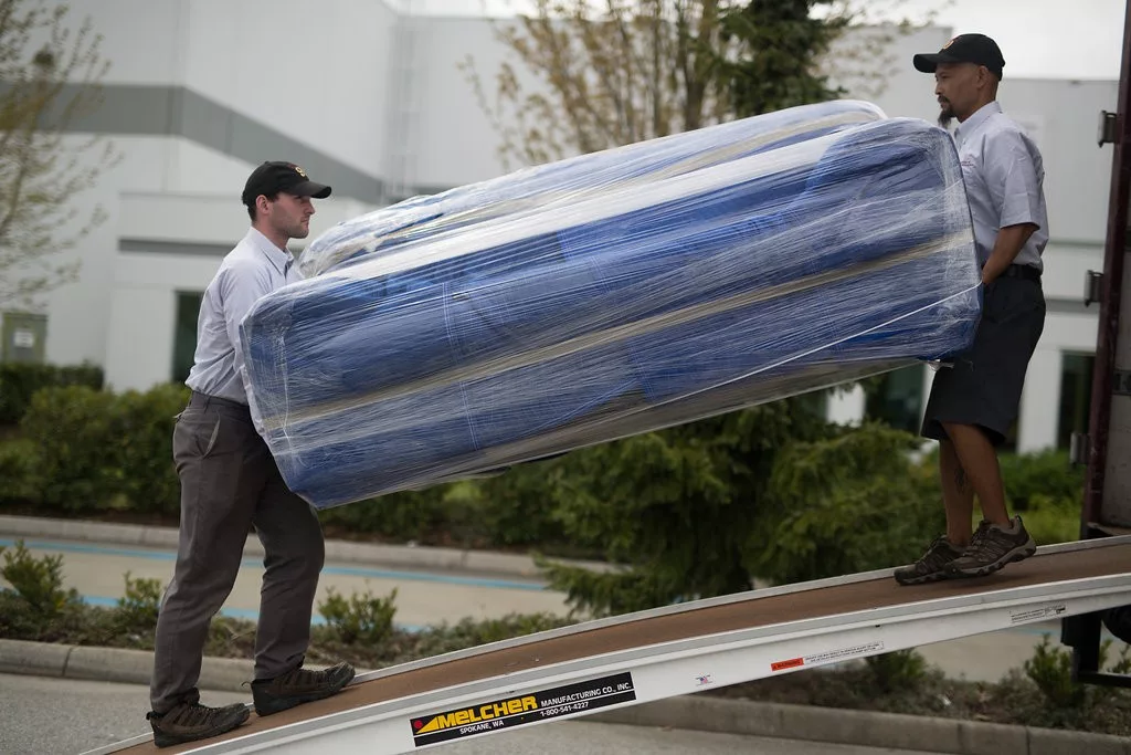 Two T-R staff in uniform are moving a couch into a Tippet-Richardson parked moving truck using a Melcher ramp