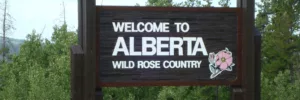 Wooden Alberta tourism logo sign that displays Welcome to Alberta Wild Rose Country