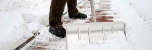 Man, wearing a brown pair of pants and black shoes is shoveling snow off his pathway to his front door