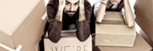 Distressed couple kneeled down surrounded by moving boxes with their hands to their heads