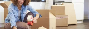 Lady wearing a blue shirt taping up boxes to move her belongings