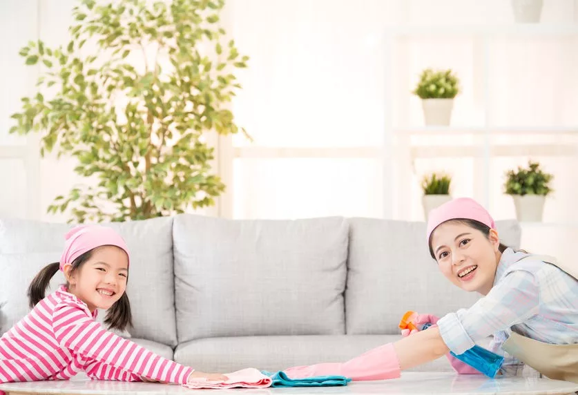 Asian mother and daughter wearing a pink cap wiping a table