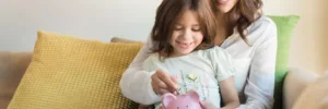 Lady with her daughter sitting on a couch holding a pink piggy bank