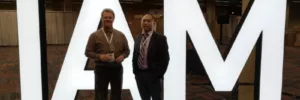 Two men in front of a white IAM conference logo representing Tippet-Richardson